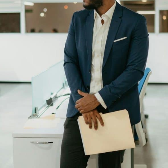 A person in a blue blazer standing in an office holding a folder.