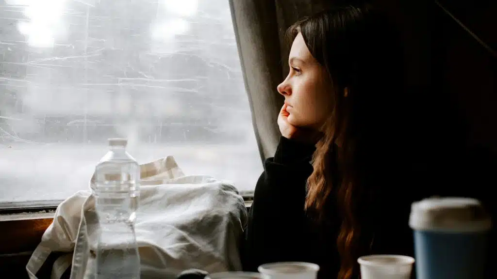 A woman sitting at a table having coffee and looking outside the window.