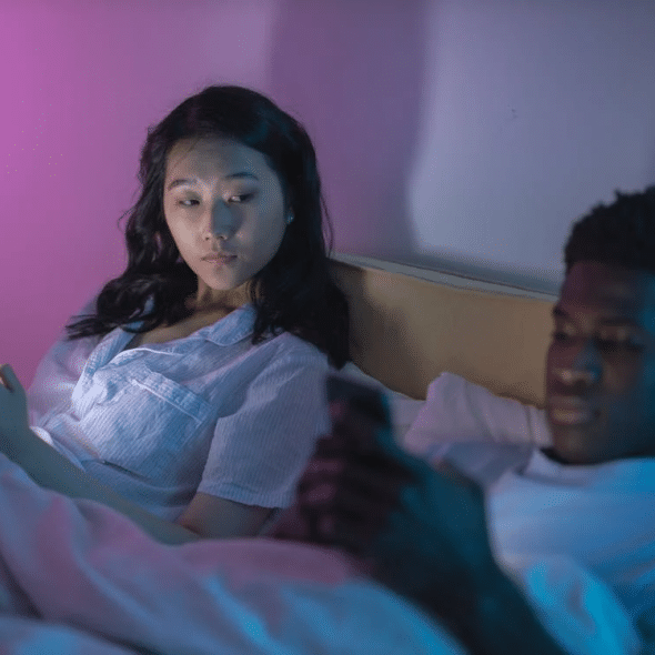 Couple in bed on phones ignoring each other