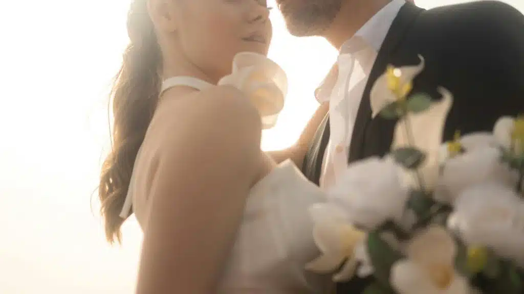 A bride and groom embrace softly in warm sunlight.