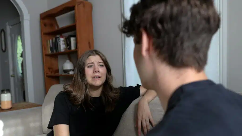 A woman looking at a man as they sit on a couch.