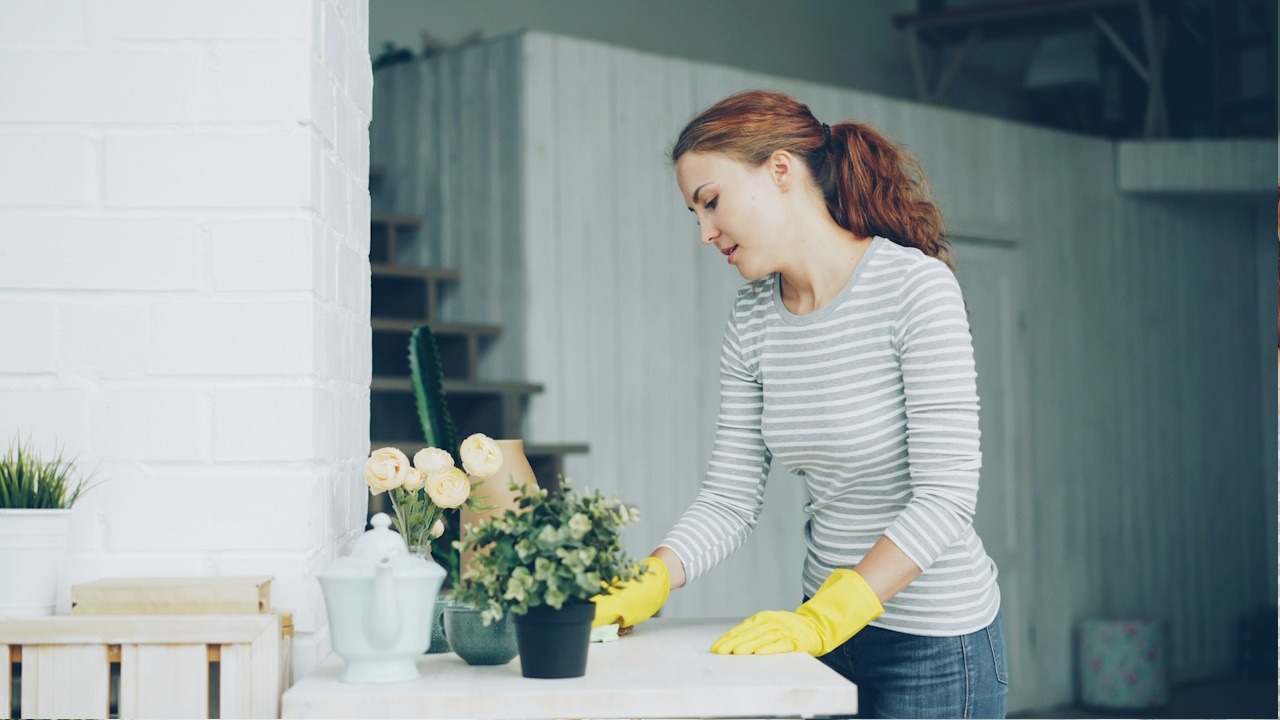 A woman wearing rubber gloves cleaning a table’s surface.