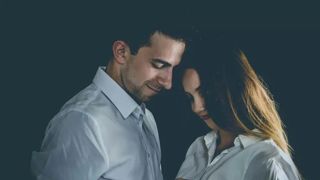 A couple standing near to each other and smiling while looking downwards.