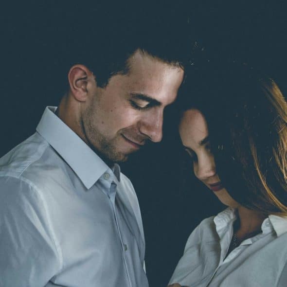A couple standing near to each other and smiling while looking downwards.