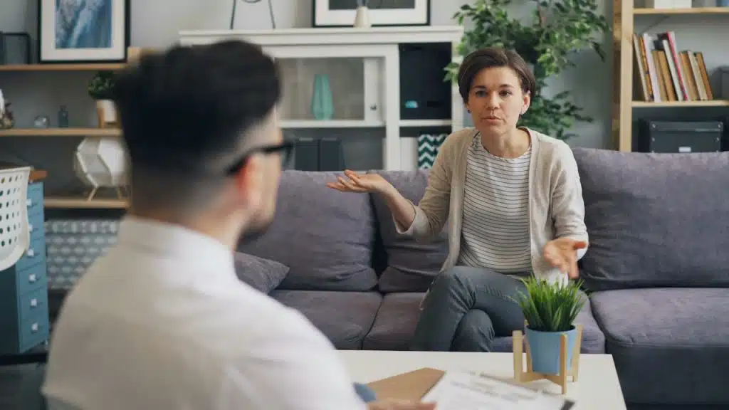 A woman arguing with a man as she sits on a couch.