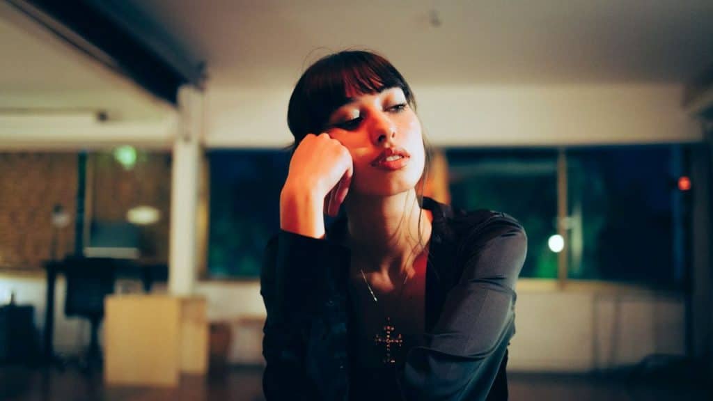 A woman with dark hair and bangs rests her chin on her hand while looking away.