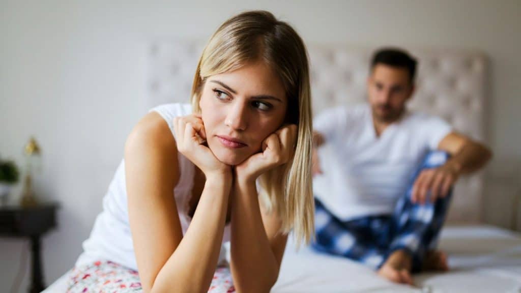 A woman rests her chin on her hands while a man sits blurred in the background.