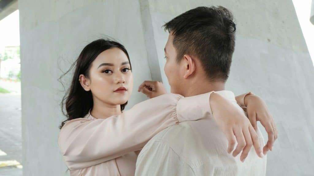 A woman with her arms around a man's neck looks directly into the camera.