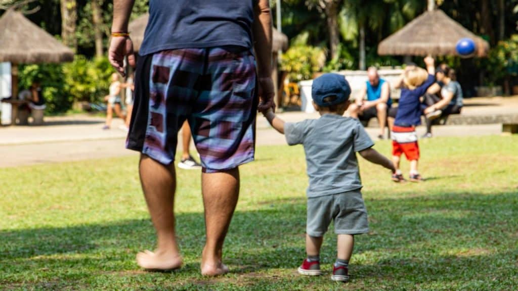A man walking barefoot on grass holding a child's hand.