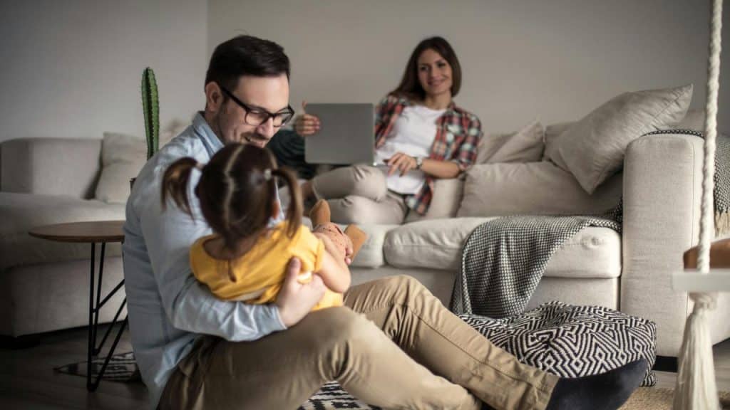 A father holding his daughter on the floor as the mother watches from the couch.