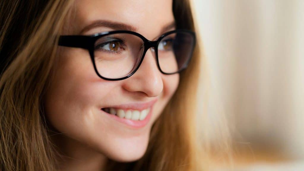 A woman wearing glasses smiling brightly.