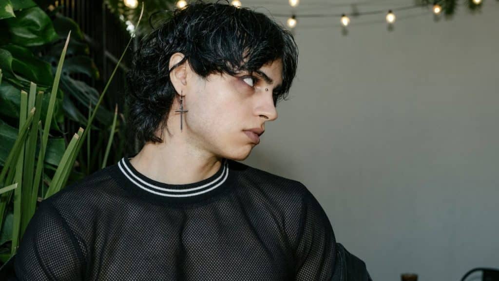 A person with dark hair and a cross earring looks away against a background of string lights.