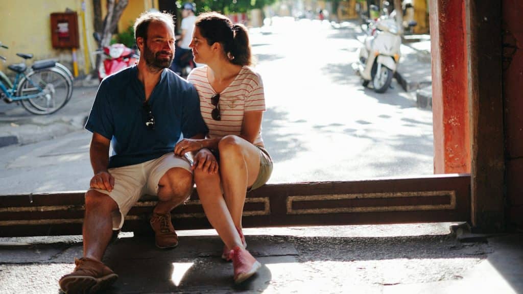 A couple sitting on a bench in a sunny street.