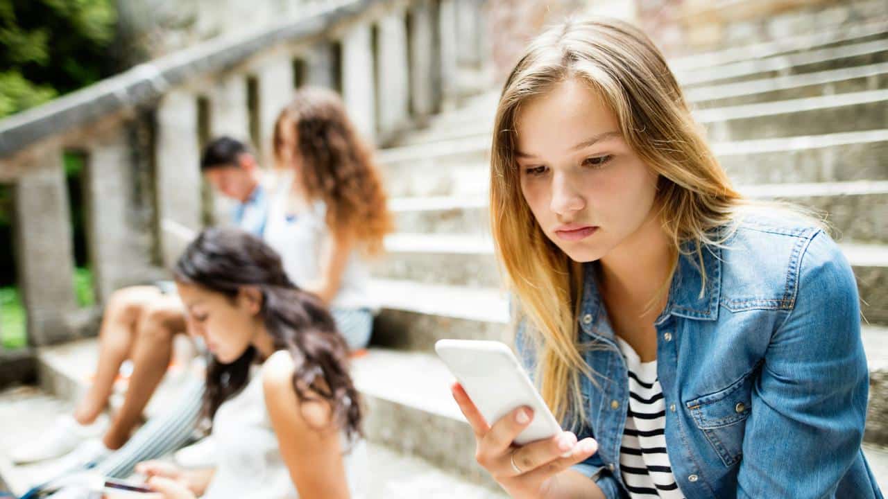 A teenage girl sitting on outdoor steps, looking at her smartphone.