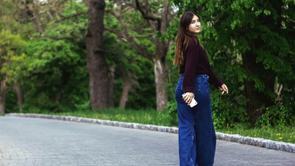 A woman in a dark sweater and blue jeans walks away while looking back over her shoulder.