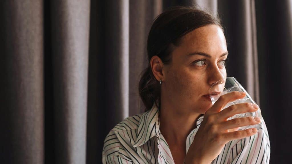 A woman holding a glass of water and looking off to the side.