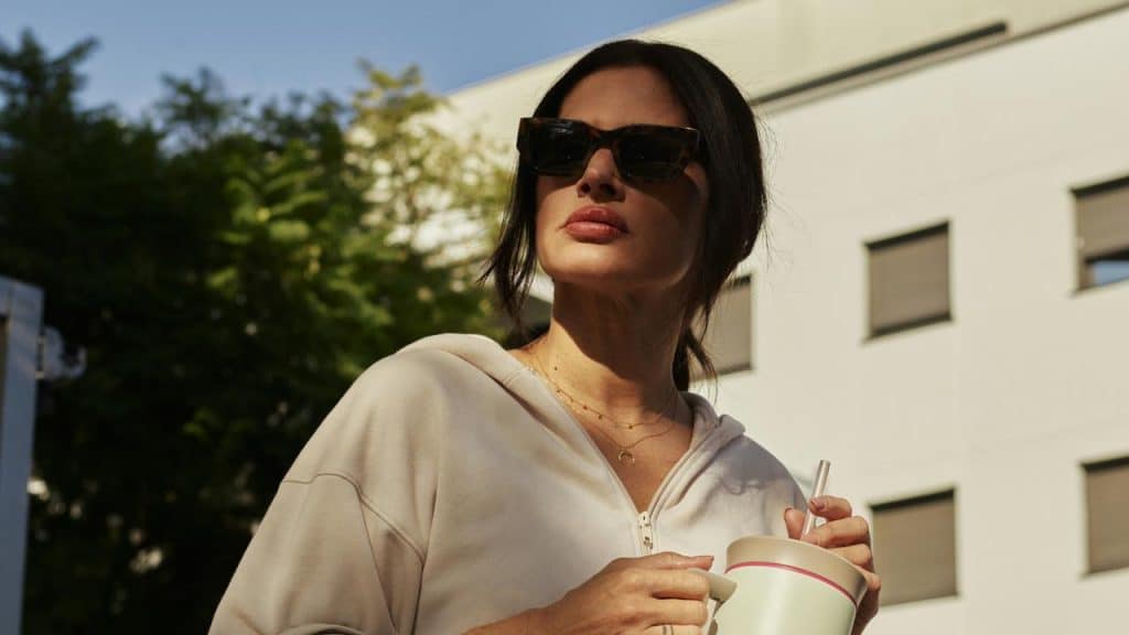 A woman wearing sunglasses holding a drink outdoors.