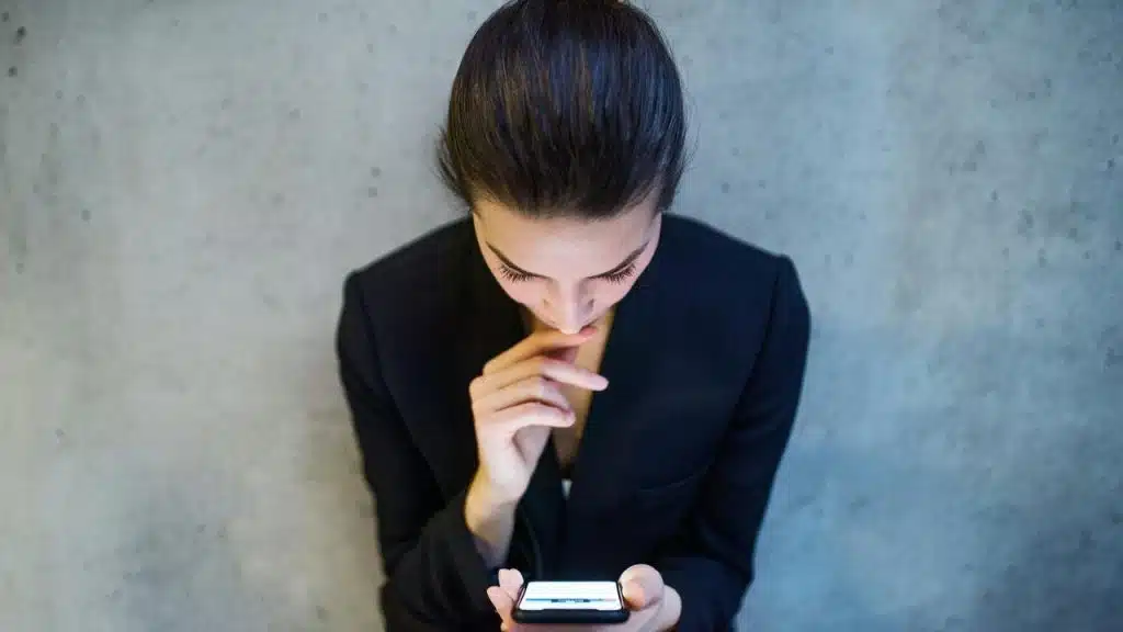 A woman in a dark blazer looking down at her phone thoughtfully.