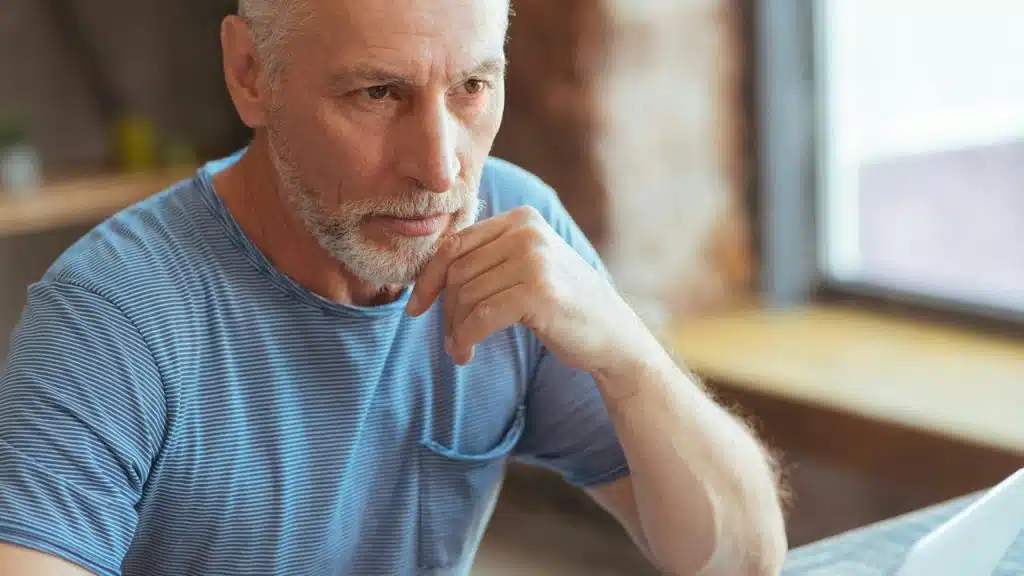 An older bearded man resting his chin on his hand, looking pensive.