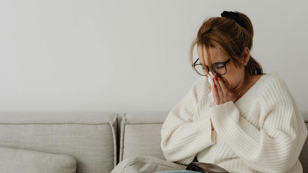 A person sitting on a couch, holding their hands over their face.