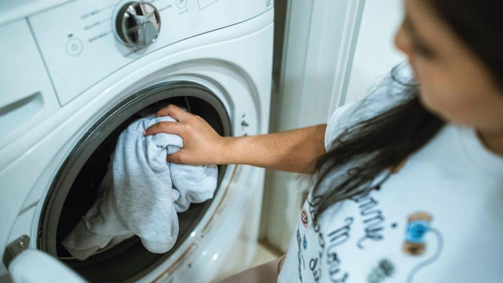 A person loading clothes into a front-loading washing machine.