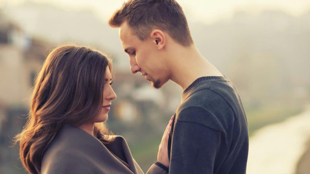 A couple standing close together, gazing at each other outdoors.