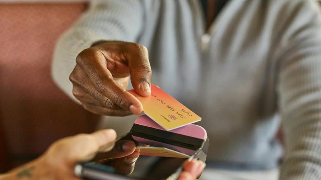 A person holding a credit card near a mobile payment device.