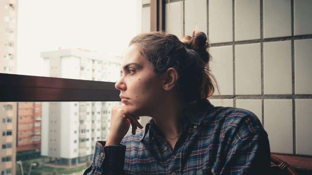 A woman in a plaid shirt rests her chin on her hand, looking out a window.
