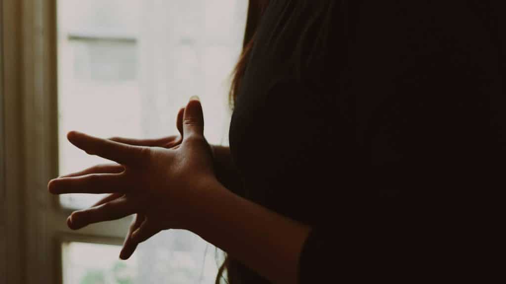 A close-up of hands gently clasped near a softly lit window.