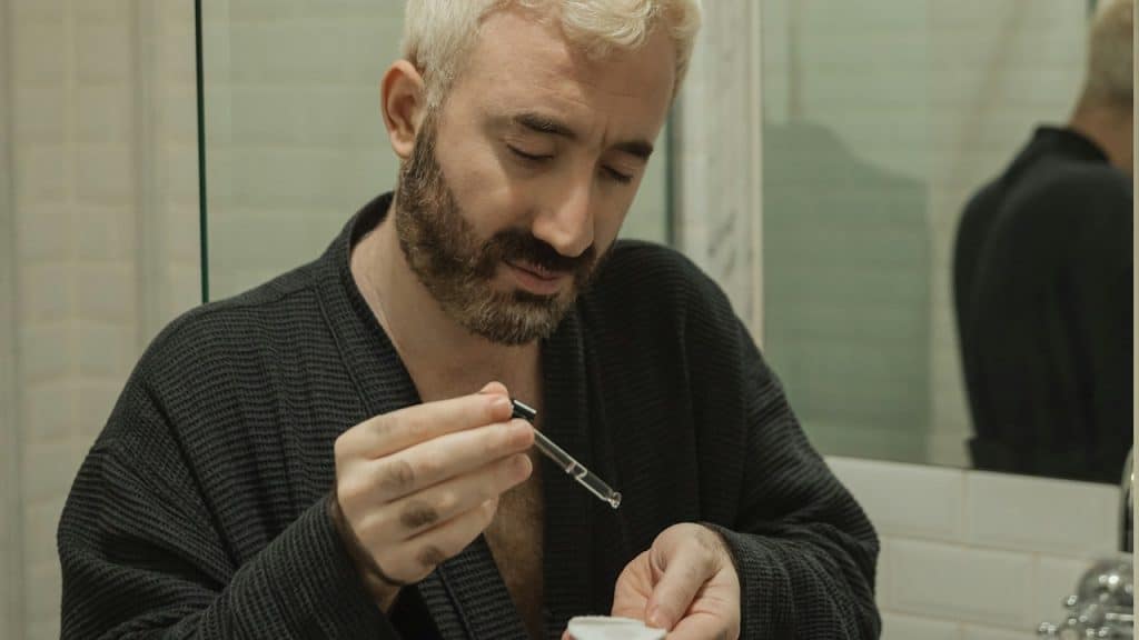 A man standing in a bathroom holding a dropper.