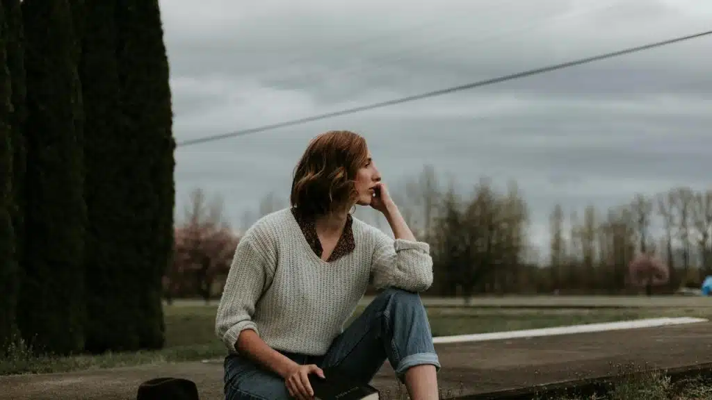 A person sitting outdoors gazing into the distance under a cloudy sky.