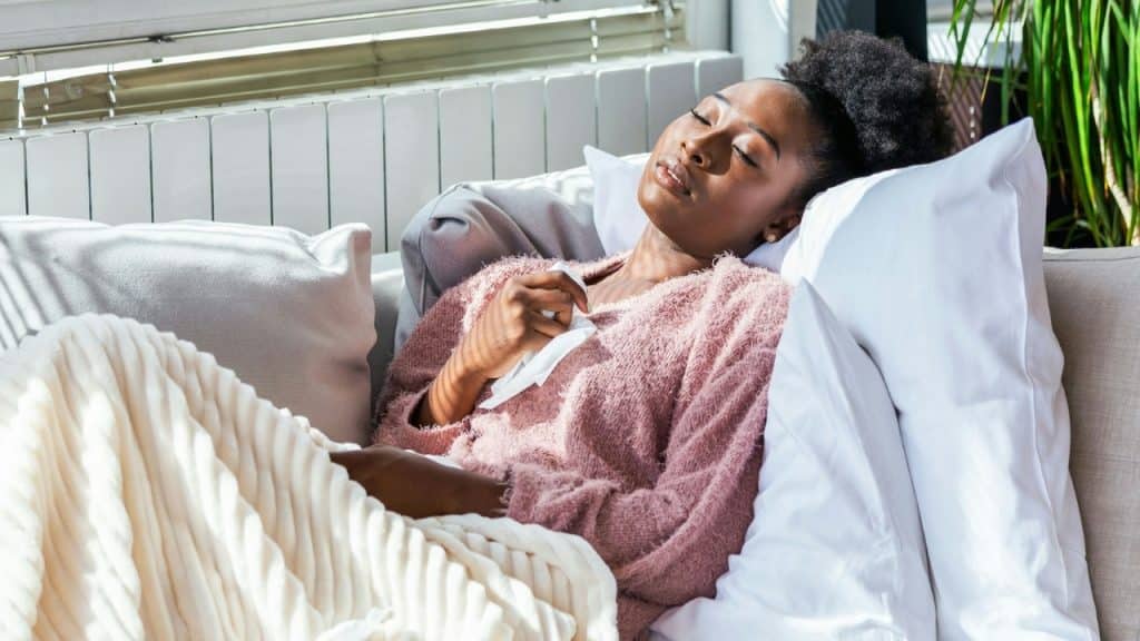 A woman with her eyes closed lies on a couch holding a white tissue to her chest.