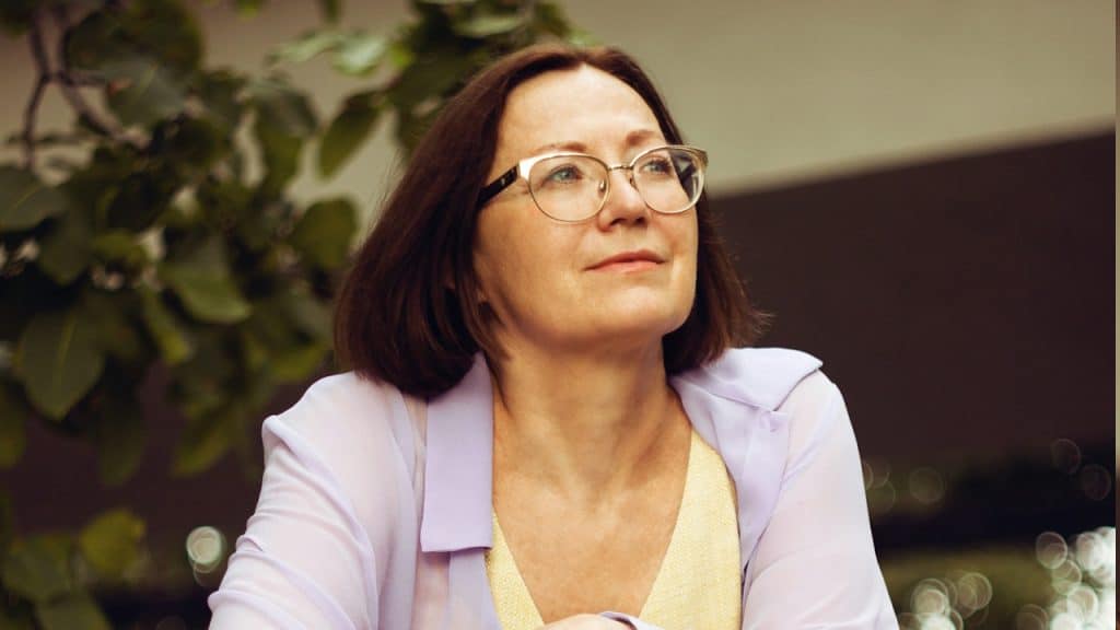 A woman in a white blazer and yellow dress shirt.