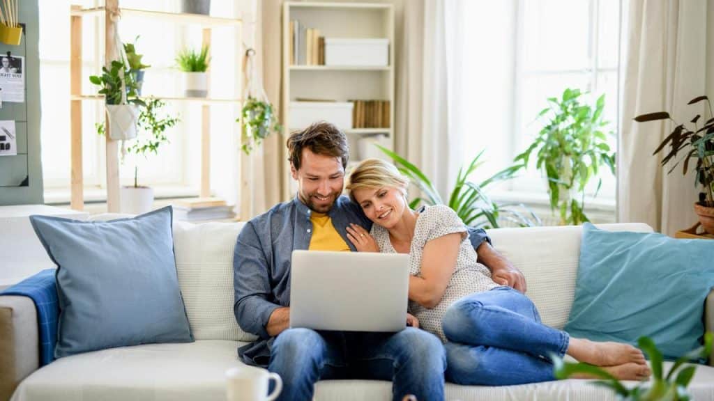 A couple relaxing on a sofa while looking at a laptop together.