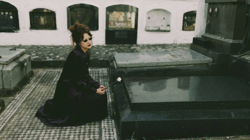A woman kneels-at-a-tomb-in-a-cemetery.