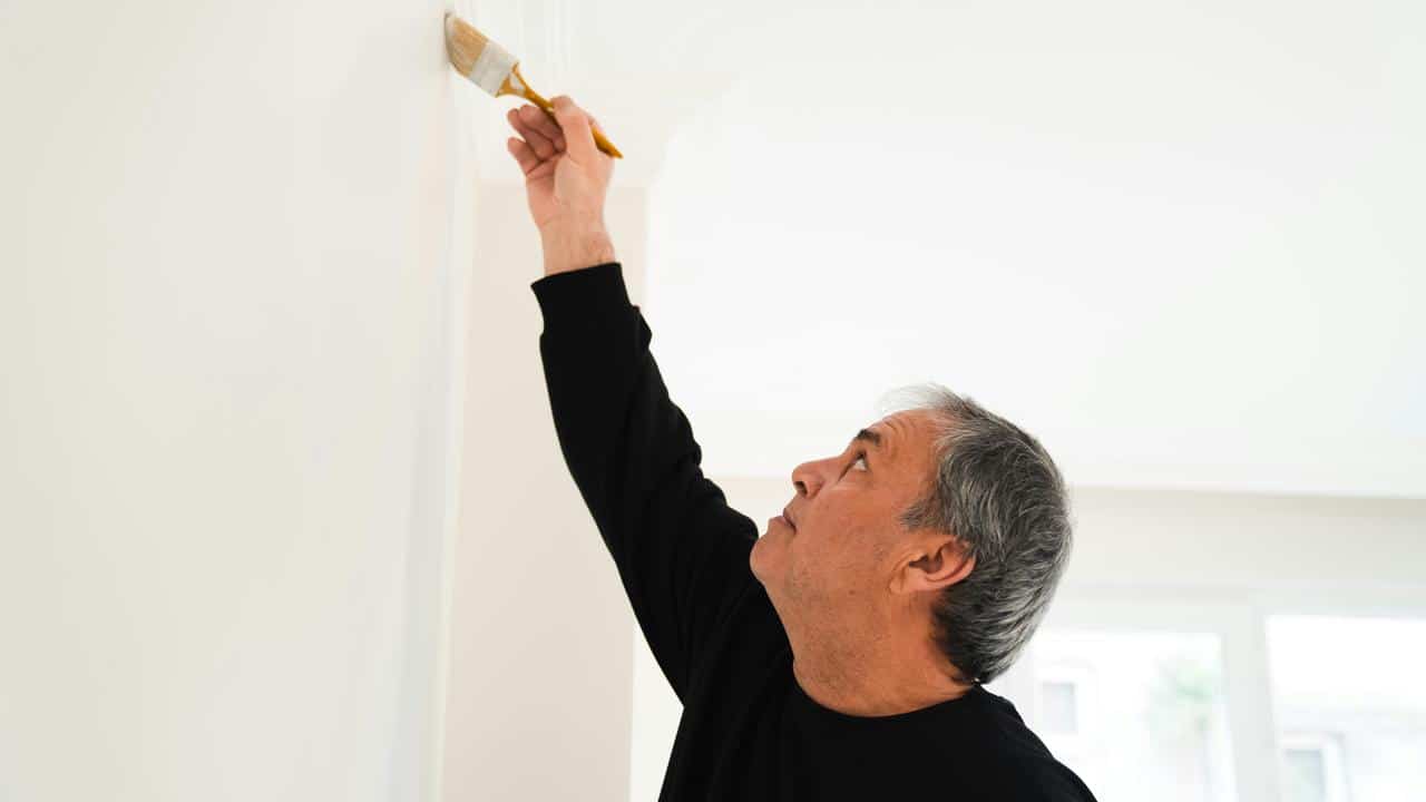 A man painting a wall trim with a brush.