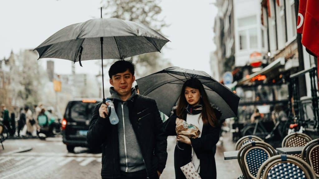 A man and woman walk down a city street in the rain, each holding black umbrellas.