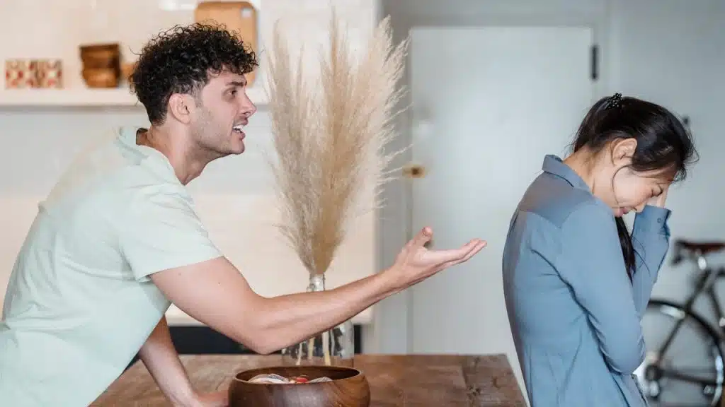 A man is aggressively yelling and gesturing at a woman who is turned away from him.