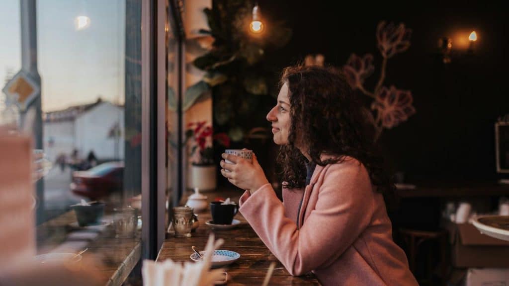 A woman holding a cup and gazing out a café window.