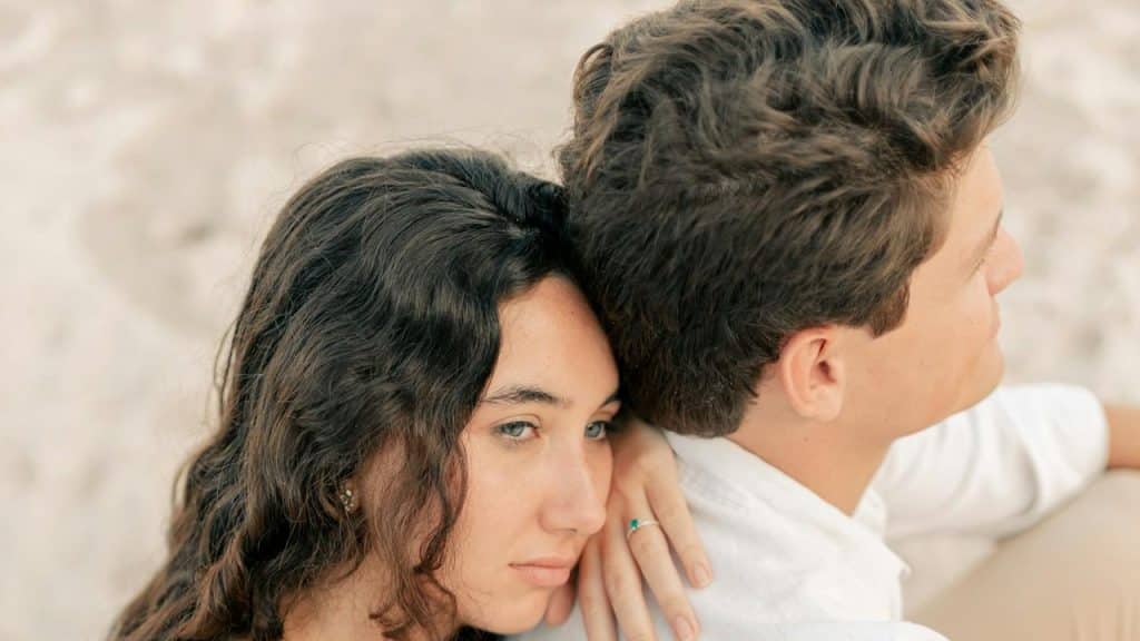 A woman with a forlorn expression leaning on a man’s back.
