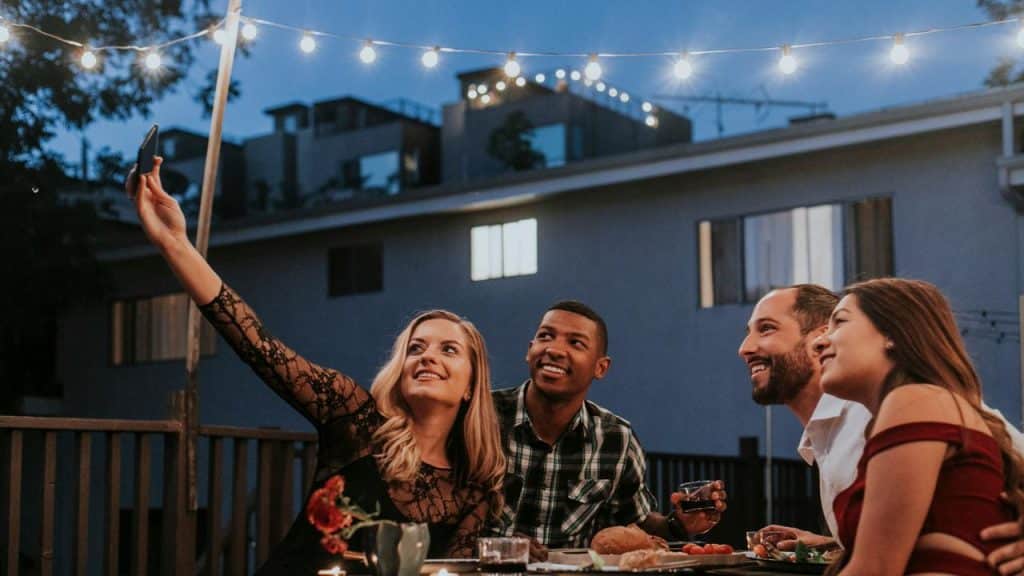 A group of friends taking a selfie at an outdoor dinner under string lights.