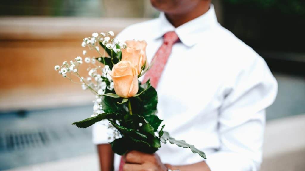A person wearing a white shirt and red tie holds a bouquet of light orange roses.