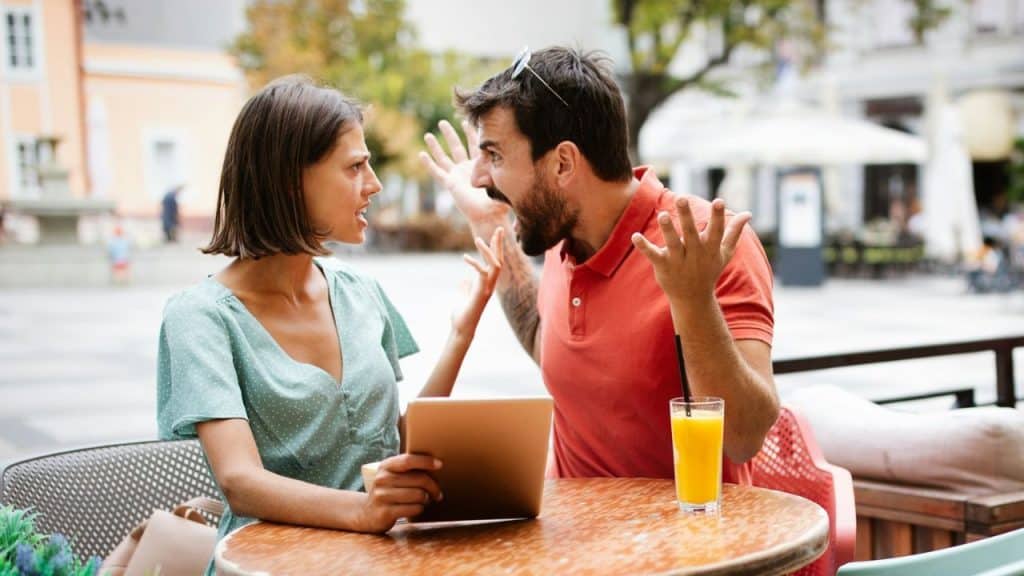 A man and woman shout at each other while sitting at an outdoor cafe table.