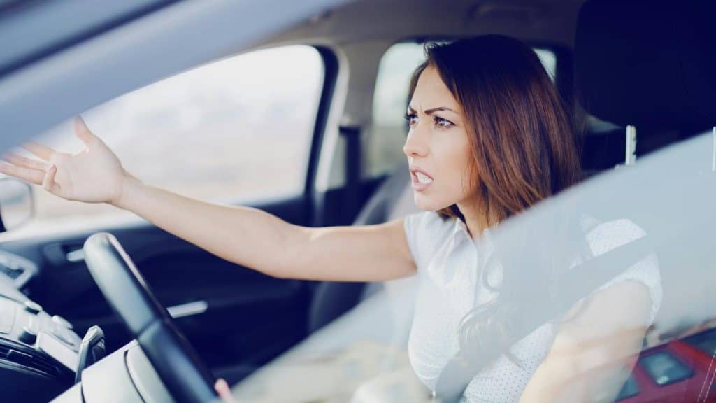 A woman in a car gesturing angrily while driving.