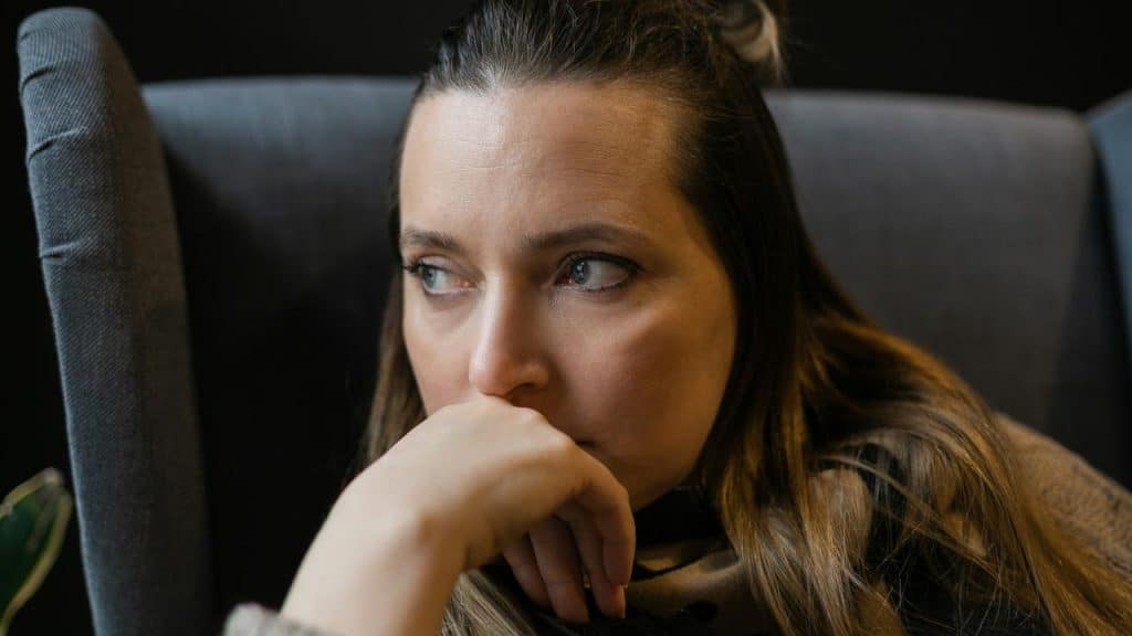 A woman sitting in a chair with her hand near her face looking pensive.