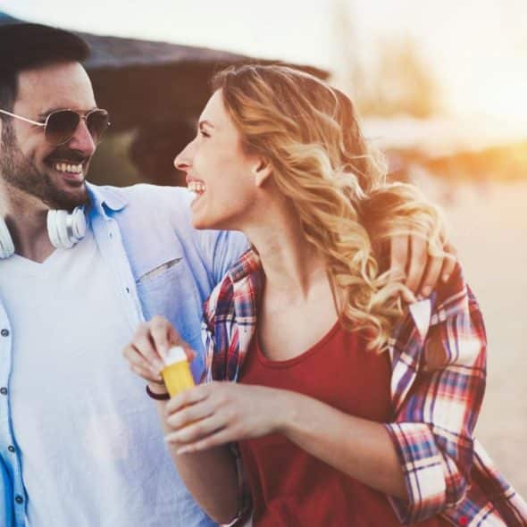 A smiling man and woman walk outdoors together while holding a colorful beach ball.