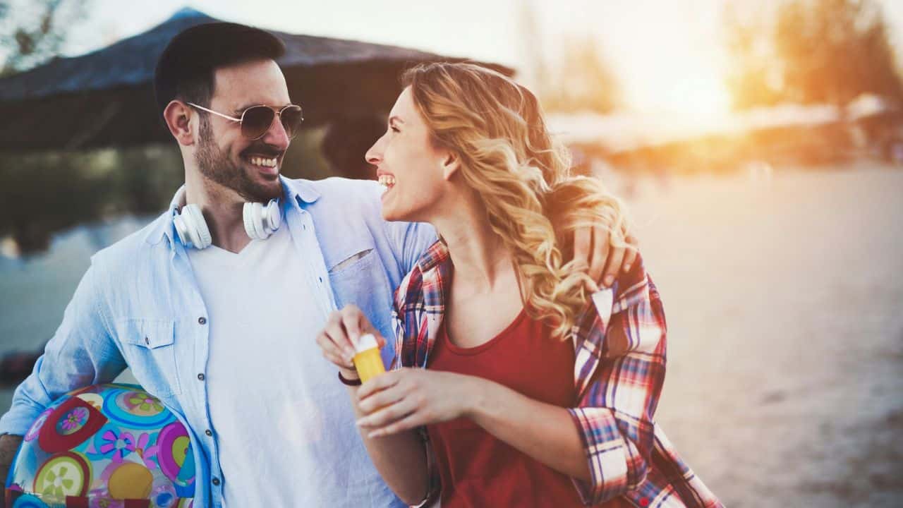 A smiling man and woman walk outdoors together while holding a colorful beach ball.