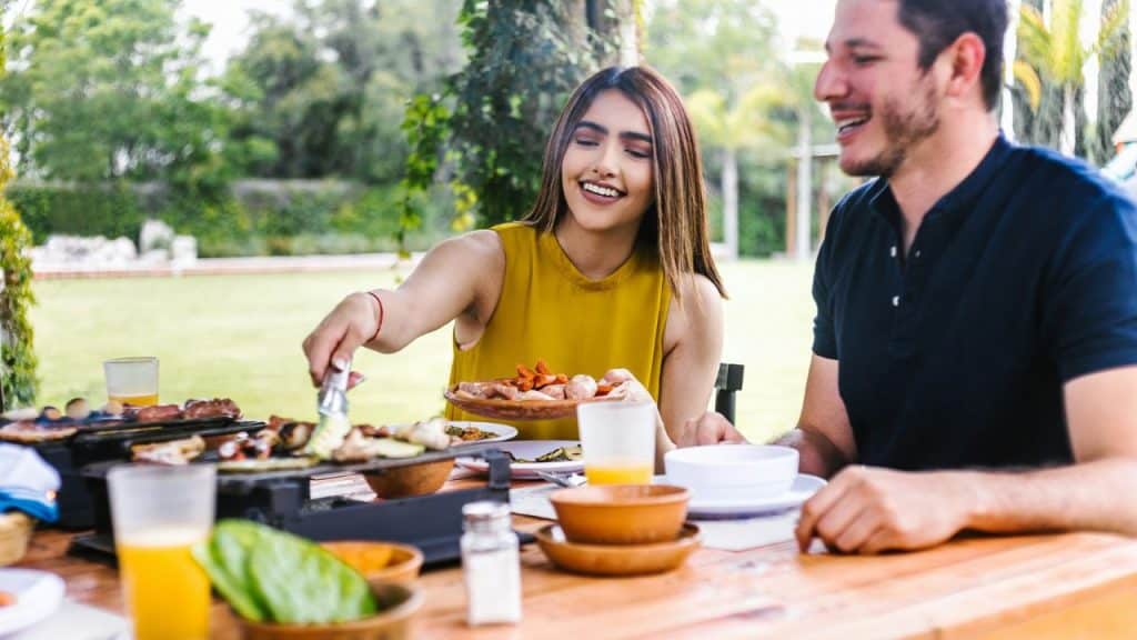 A woman uses tongs to serve food from a grill during an outdoor daytime meal.