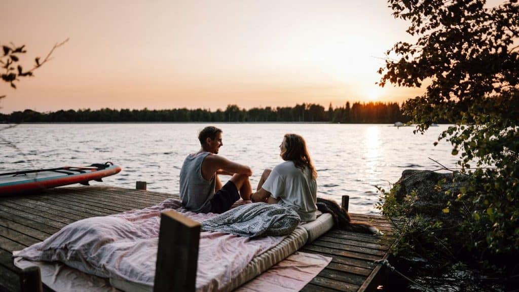 A couple sitting on a dock by the lake at sunset.