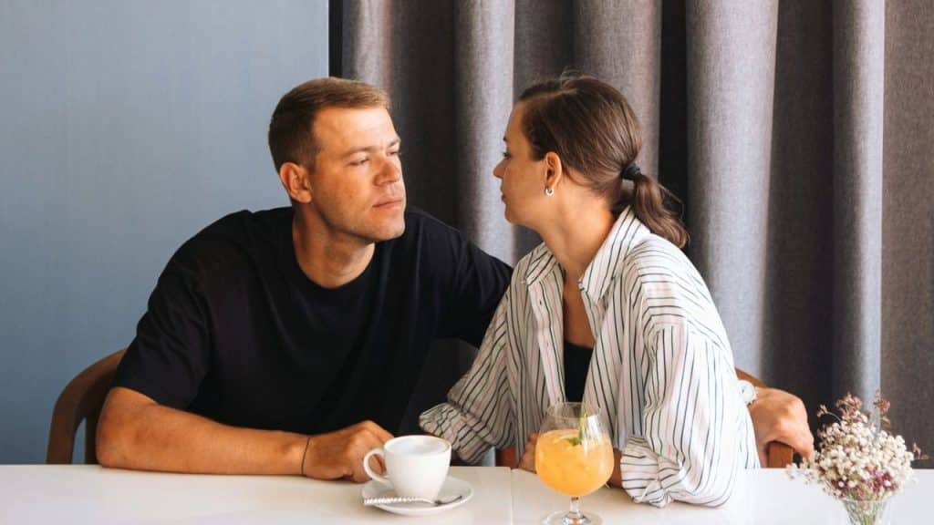 A man in a black shirt and a woman in a striped shirt sit at a table.